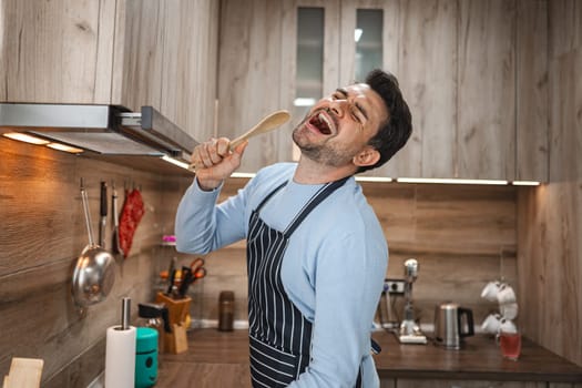 Brown-haired man sings cheerfully into a wooden stove in the kitchen while cooking.
