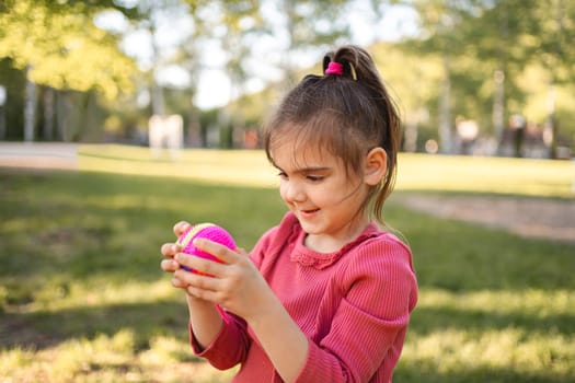 Cute little girl is holding a ball on the playground.