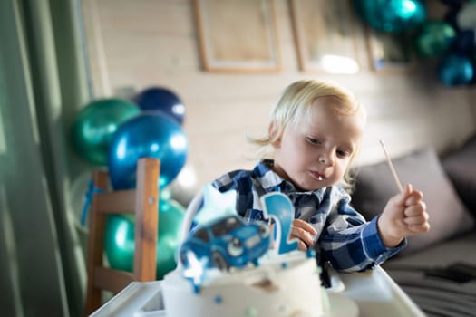 A young child is focused on a cake decorated with a car design, seated at a table in a warmly decorated indoor space filled with colorful balloons.