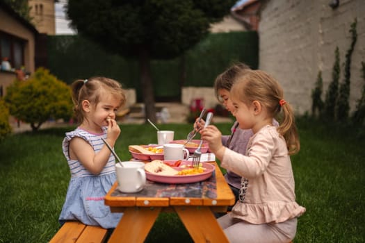Kids enjoy a cheerful lunch outside under the warm sun and green trees.
