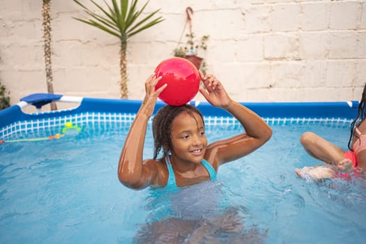 A girl enjoys playful moments with a red ball in the pool.