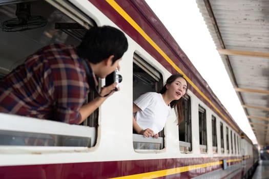 A man enthusiastically photographs his partner who is playfully leaning out of the train window, embodying the spirit of adventure and spontaneity.