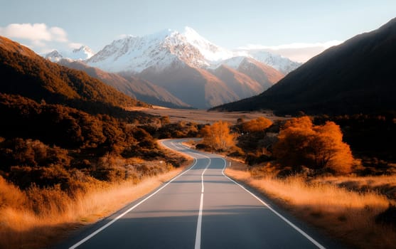 Serene mountain road with autumn trees leading to snow-capped peaks.