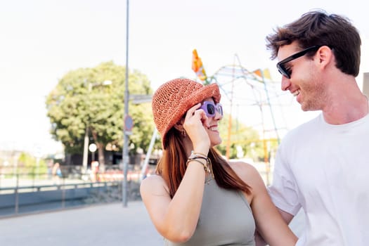 young couple smiling happy looking each other, the woman is wearing a hat and sunglasses, concept of youth and romance, copyspace for text