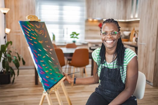An artist joyfully showcases her vibrant artwork in a cozy workspace.
