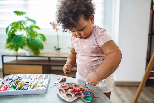 A curious toddler joyfully experiments with paints at a table.