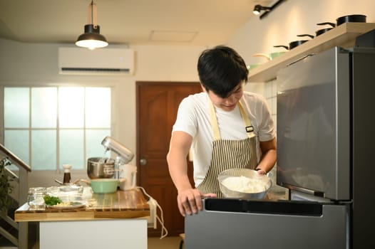 Smiling man places a bowl of homemade whipped cream into the refrigerator.