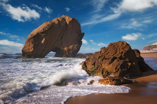 Penedo do Guincho, a large boulder rock arch at Praia da Santa Cruz, Portugal, with ocean waves and sandy beach