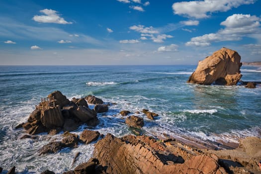 Penedo do Guincho, a large boulder rock arch at Praia da Santa Cruz, Portugal, with ocean waves and sandy beach