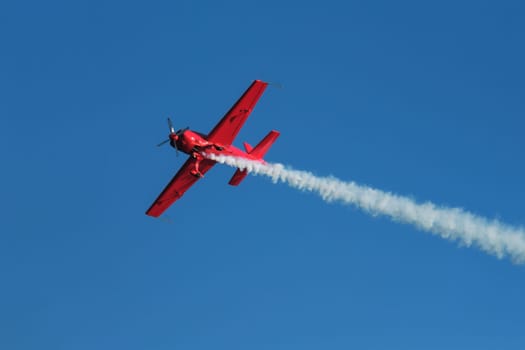 Red stunt aerobatic plane performing stunts in blue sky. Concept of speed, difficulty, precision, risk