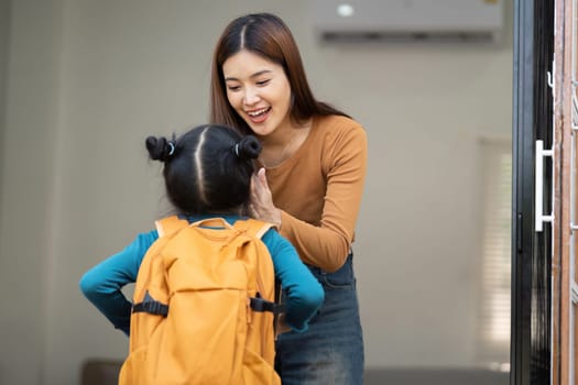 A loving mother greets her daughter with a warm smile while the girl, clad in her school outfit, appears excited about the day ahead.