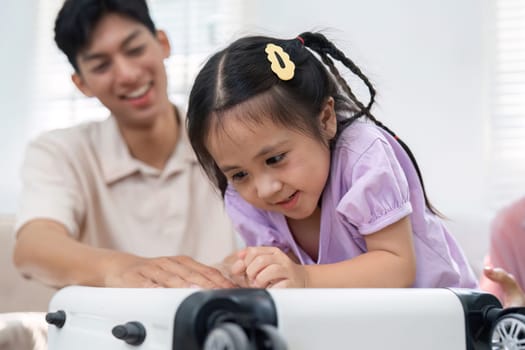 A father encourages his daughter as she playfully investigates a suitcase, showcasing a loving and supportive family moment in a cozy living room.