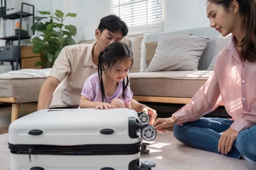 A playful daughter interacts with a suitcase while her parents assist her, highlighting the joy of family life in a relaxed home setting.