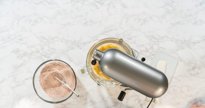 Overhead setup with an electric mixer and bowls of prepared dry and wet ingredients for Pale Gingerbread Cookies with Subtle Spice Flavor. A whisk rests in the flour mixture, ready to combine ingredients in the mixer.