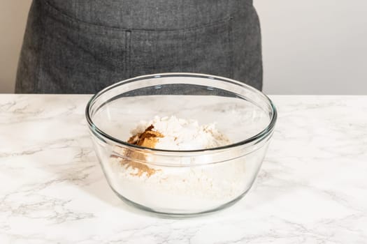 Eye-level view of a mixing bowl containing dry ingredients for Classic Gingerbread Cookie Dough, including flour, baking powder, and spices like cinnamon, ginger, and cloves. These ingredients are ready to be combined, forming the base for the gingerbread dough.