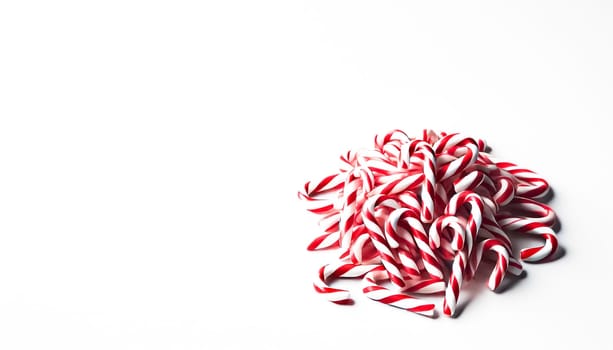 A small pile of neatly rearranged red and white striped candy canes viewed from a slightly elevated angle on a plain white background. This organized heap highlights the candy canes' colorful and festive appearance while maintaining a playful and casual feel.