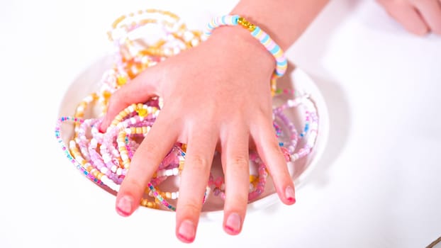 Delicate fingers of a young girl navigate through a treasure trove of bright, multicolored beads, each compartment revealing a new hue to choose from. She's immersed in the joyful task of stringing together a handmade bracelet, with golden beads and pearls lying nearby to add a touch of sparkle to her creation.