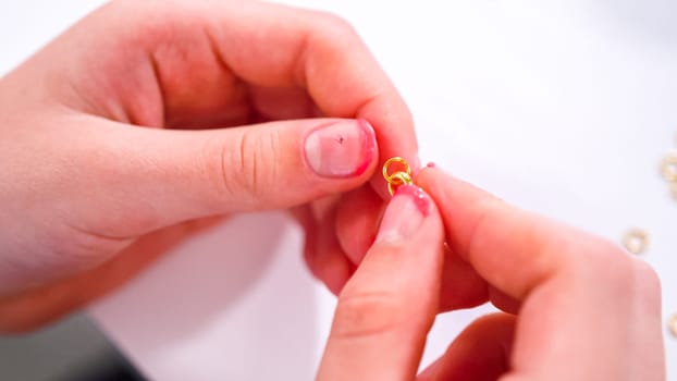 Delicate fingers of a young girl navigate through a treasure trove of bright, multicolored beads, each compartment revealing a new hue to choose from. She's immersed in the joyful task of stringing together a handmade bracelet, with golden beads and pearls lying nearby to add a touch of sparkle to her creation.