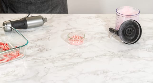 Castle Rock, Colorado, USA-November 26, 2024-A food processor with crushed candy canes displayed alongside a small glass bowl of finely crushed candy and uncrushed candy canes in a larger container, on a marble countertop.