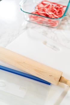 Castle Rock, Colorado, USA-November 26, 2024-A rolling pin placed on a plastic zip-top bag, set on a marble countertop next to a container of candy canes, preparing for crushing into fine pieces for baking recipes.