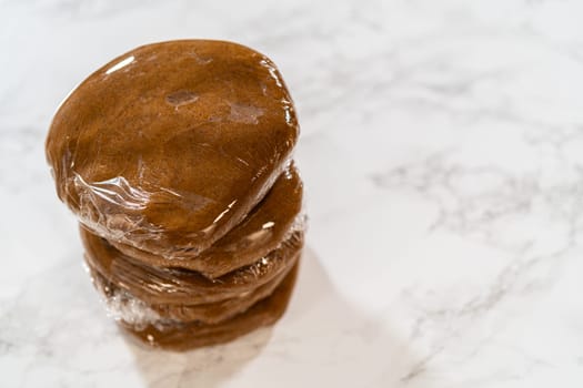 Stacked portions of Spiced Gingerbread Cookie Dough Perfect for Baking wrapped in plastic wrap. The dough is divided for easy handling and chilled, ready for rolling and shaping into cookies.