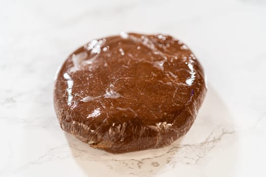 A ball of Chocolate Gingerbread Cookie Dough wrapped in plastic wrap, ready to be chilled. This chilling step helps the dough firm up, making it easier to shape and bake.