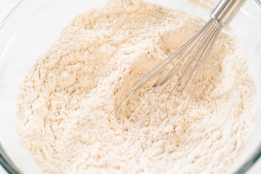 Close-up view of flour being whisked in a glass bowl, part of the initial steps in preparing Classic Gingerbread Cookie Dough. The whisk helps to evenly mix the dry ingredients before combining with wet ingredients.