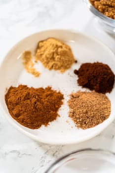 A white bowl containing the aromatic spices for Chocolate Gingerbread Cookie Dough, including cinnamon, ground ginger, cloves, and cocoa powder. These spices will infuse the dough with warm and rich flavors.