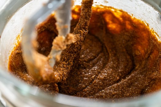 The mixer bowl shows a rich, dark molasses added to the creamed butter and sugar. The molasses is beginning to integrate, creating a deep brown, aromatic mixture.