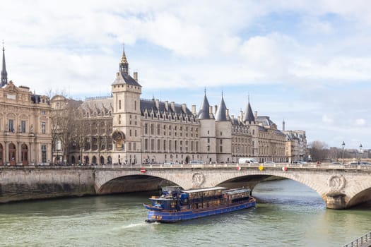 Paris, France - February, 23rd 2025: View of Conciergerie Castle and Bridge of Change over river Seine with beautiful touristic boat. Castle is a former prison, located on west of the Cite Island