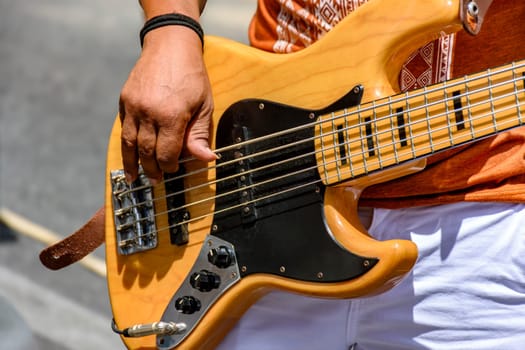 Hands playing an electric bass guitar on the street in a sunny day