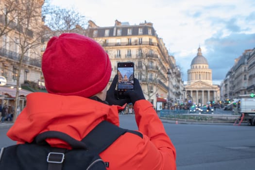 A lonely tourist in red coat takes a photo by his smartphone of the Pantheon in Paris, France, capturing its grand neoclassical architecture and timeless beauty