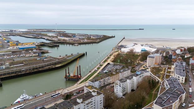 Boulogne. France 03.28.2025 Drone photo of a seaside harbor with construction barge, beach promenade, modern buildings, and residential area near the waterfront.