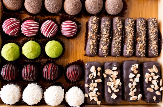 Assorted chocolate truffles and bars on a wooden tray with variety of toppings.