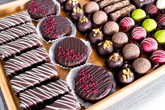 Assorted chocolate desserts with toppings on wooden tray.
