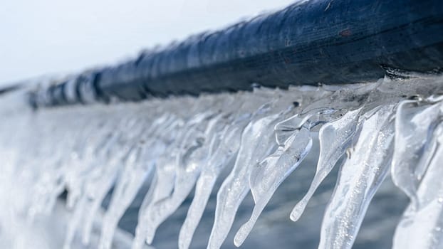 Beautiful Icicles Forming on a Metal Fence with Sunlight Creating a Sparkling Effect in Winter.