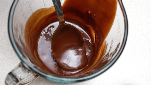 Close-up of a chocolate fudge in a glass measuring cup with a spoon.