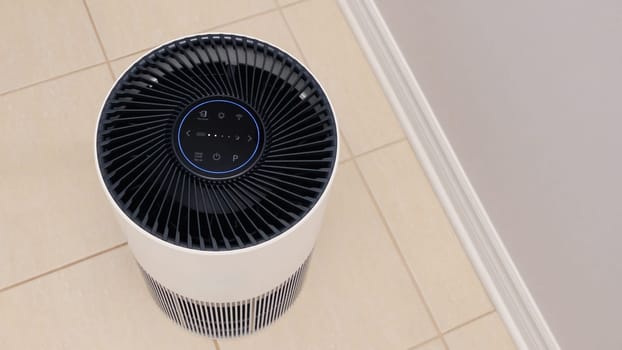 Tall round air purifier with a black top fan and a white body on a tile floor against the wall.
