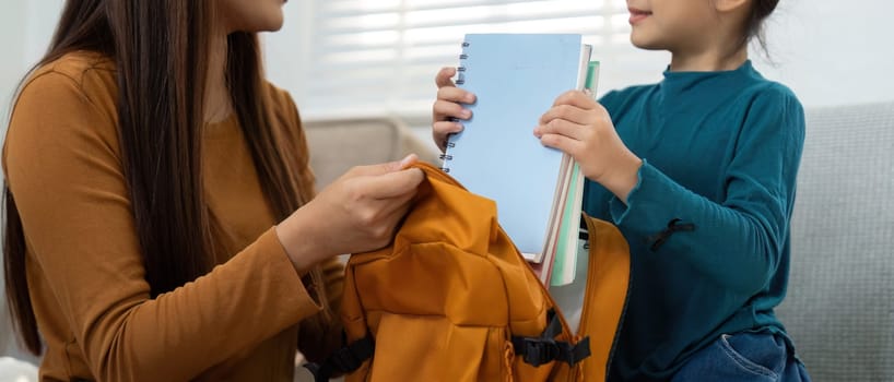 A woman helps a girl gather her school books, showcasing the importance of preparation and learning as they prepare for the school year ahead.