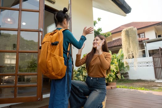 A mother joyfully waves goodbye to her daughter as she heads off to school, capturing the essence of love and encouragement.