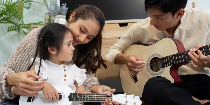 In a cozy living room, a mother lovingly teaches her daughter to play the ukulele. Their interaction emphasizes the joy of family bonding and musical learning.