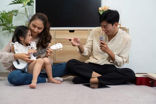 In this engaging family moment, a mother guides her daughter in playing the ukulele while the father adds joy with laughter, creating a dynamic learning experience.