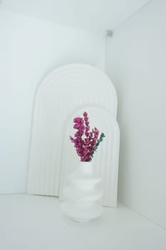 A unique vase holds pink flowers against a white background in a stylish space.