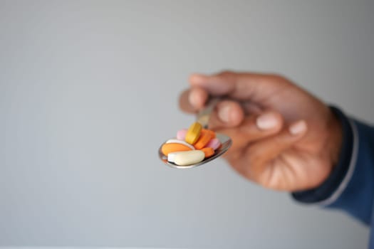 A hand offers a spoon filled with colorful vitamins and supplements.