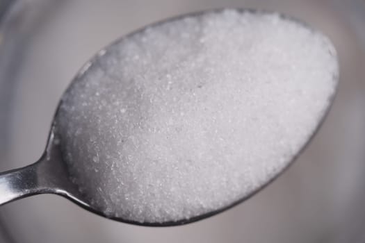 Granulated sugar rests in a metal spoon, highlighting texture and color.