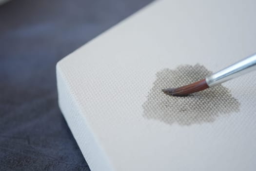 A brush gently adds gray paint on an untouched canvas surface.