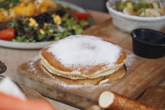 Fluffy pancakes dusted with sugar alongside fresh salad and toppings