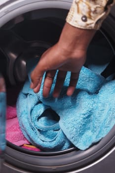 A person is loading a blue towel into a washing machine for cleaning.
