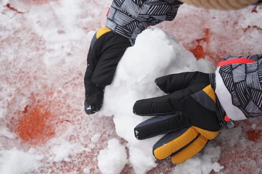 A child is forming a snowball with gloved hands in winter.