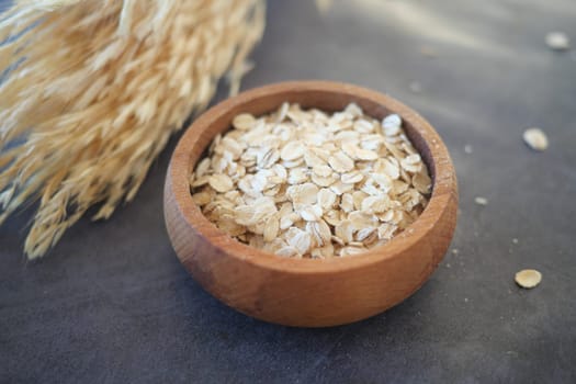 Rolled oats are displayed in a small wooden bowl beside dried grass.